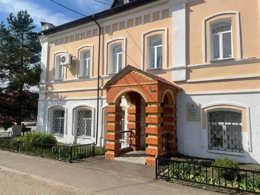 Фасад двухэтажного здания с кирпичным входом и табличкой у двери.