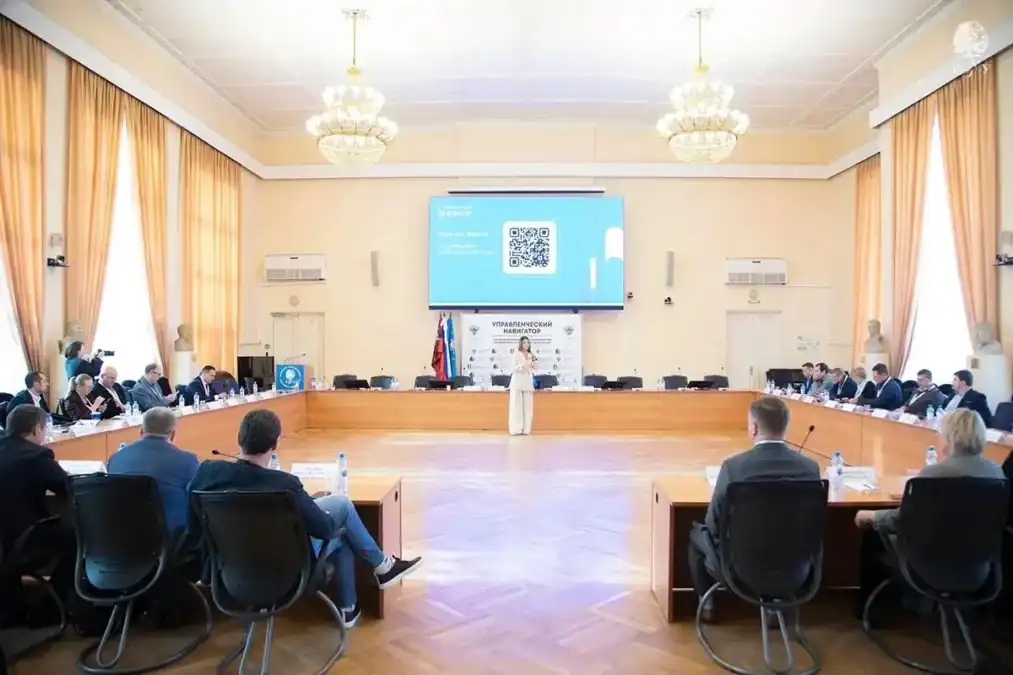 Участники программы сидят за круглым столом в большом зале заседаний.