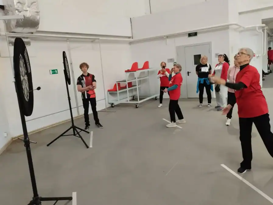 Участницы в красных футболках соревнуются в дартсе в спортивном помещении.