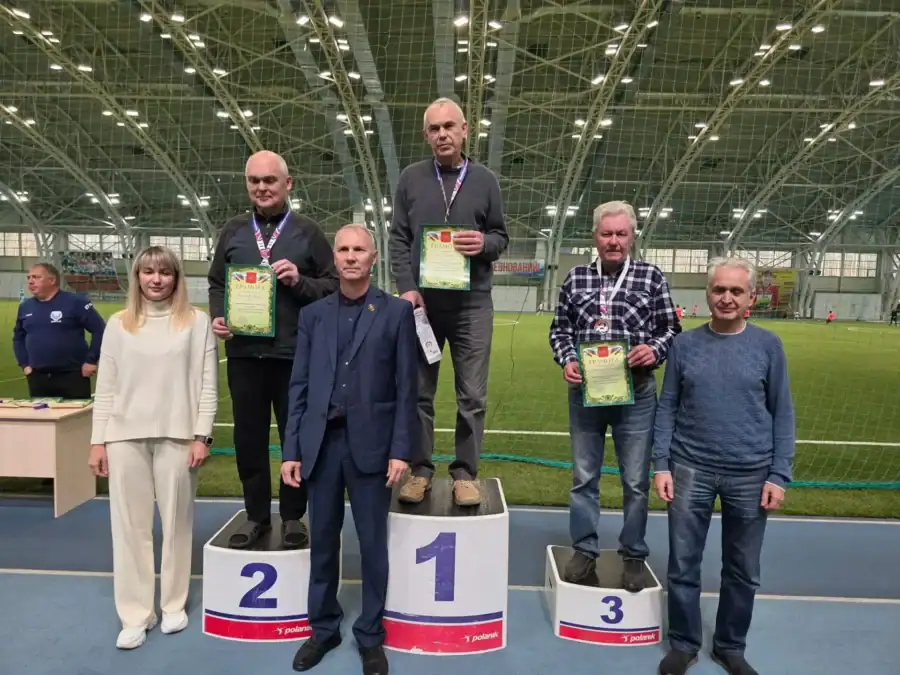 Призёры с дипломами стоят на пьедестале в крытом футбольном манеже.