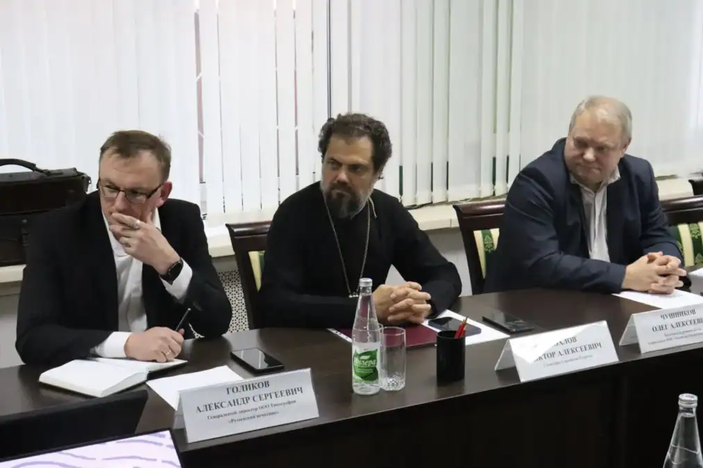 Трое участников заседания сидят за столом с документами.
