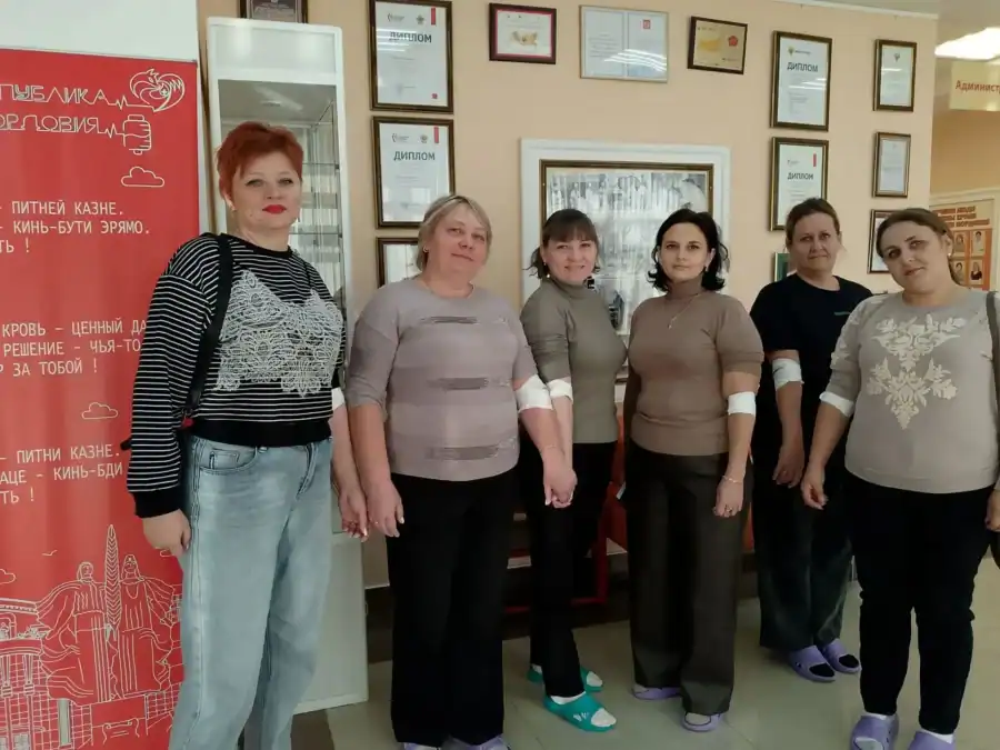 Шесть женщин с повязками на руках позируют у информационного стенда.