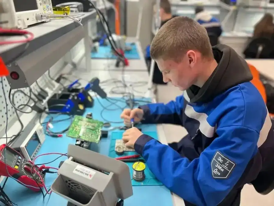 Студент паяет электронную плату за оснащённым измерительными приборами столом.
