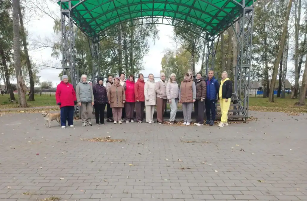 Группа людей стоит под зелёным арочным навесом в парке.