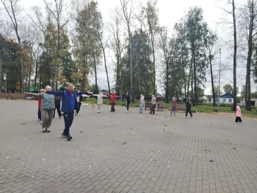 Участники утренней зарядки выполняют упражнение с разведёнными в стороны руками.