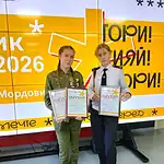 Две школьницы с дипломами стоят у экрана конкурса «Ученик года 2026».