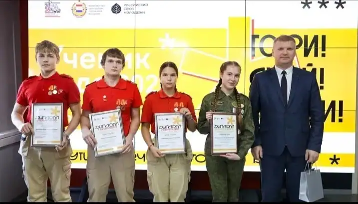 Четверо школьников с дипломами стоят рядом с мужчиной в костюме.