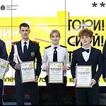Четверо участников с дипломами стоят рядом с мужчиной в костюме.