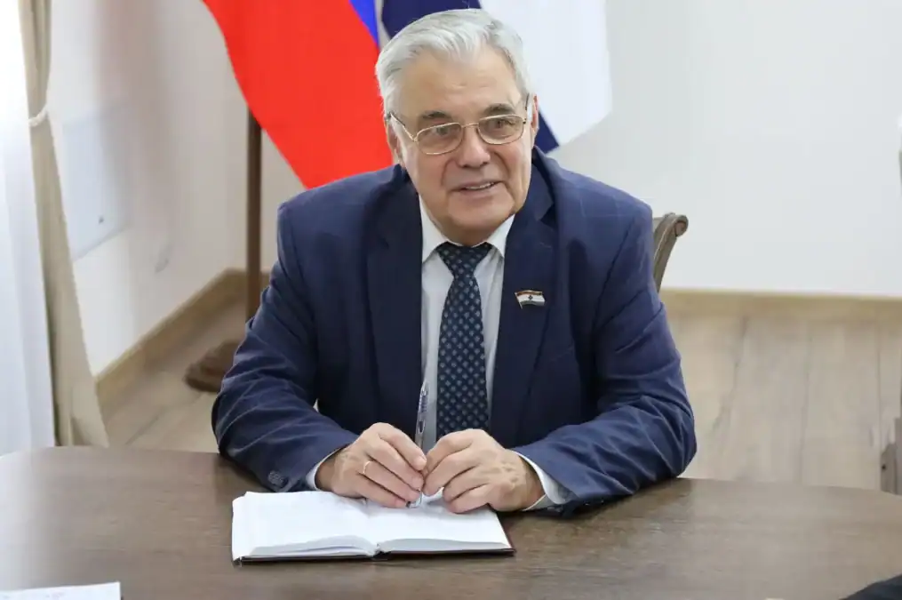 Мужчина в деловом костюме сидит за столом с открытым блокнотом.