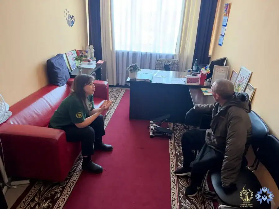 Женщина в зелёной футболке беседует с двумя мужчинами в кабинете.