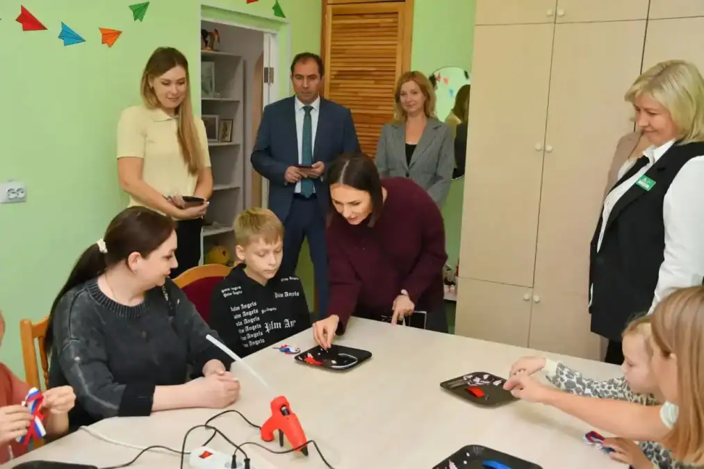 Женщина наблюдает за детьми, работающими за столом с учебными материалами.