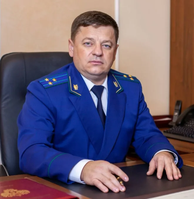Сотрудник прокуратуры в синем мундире сидит за рабочим столом в кабинете.