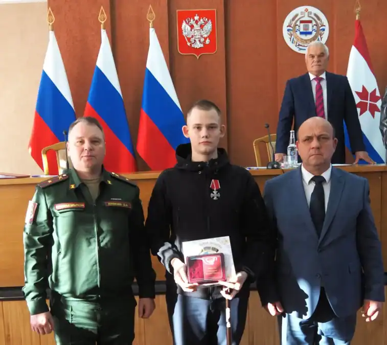 Молодой мужчина с наградой держит открытый футляр рядом с двумя мужчинами.