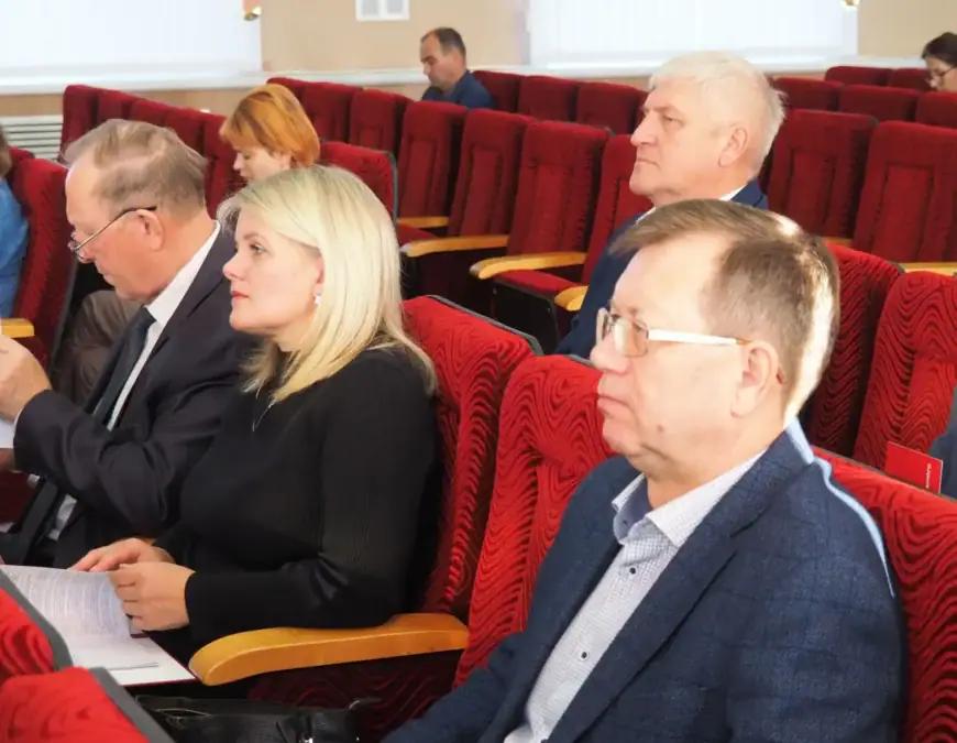 Участники заседания сидят в красных креслах с документами в руках.