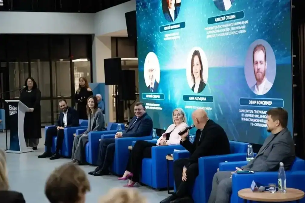 Спикеры сидят в синих креслах перед экраном с портретами наставников.