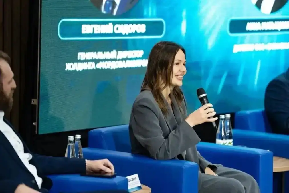 Женщина в сером костюме выступает с микрофоном во время дискуссии.