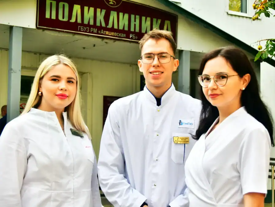 Три медицинских работника в белых халатах у входа в поликлинику.