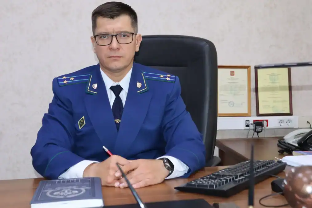 Сотрудник прокуратуры в синем форменном кителе сидит за рабочим столом.