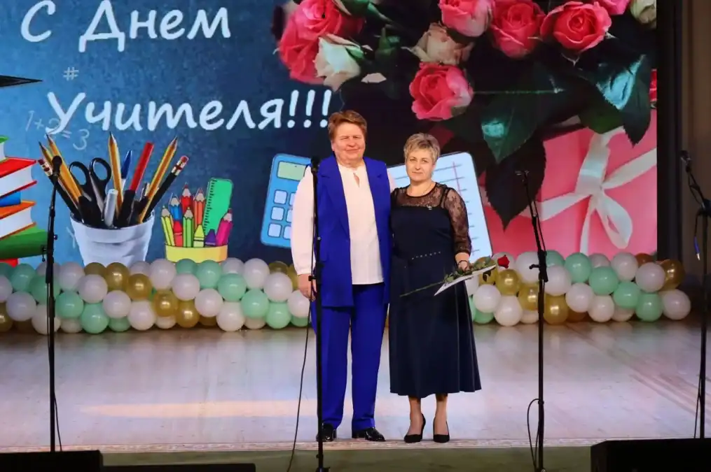 Мужчина и женщина стоят на сцене перед праздничным экраном с цветами.