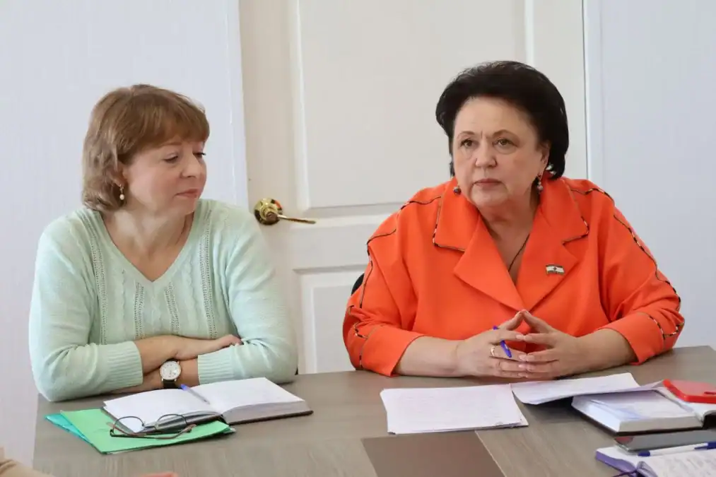 Две женщины обсуждают вопросы за столом с папками и записями.