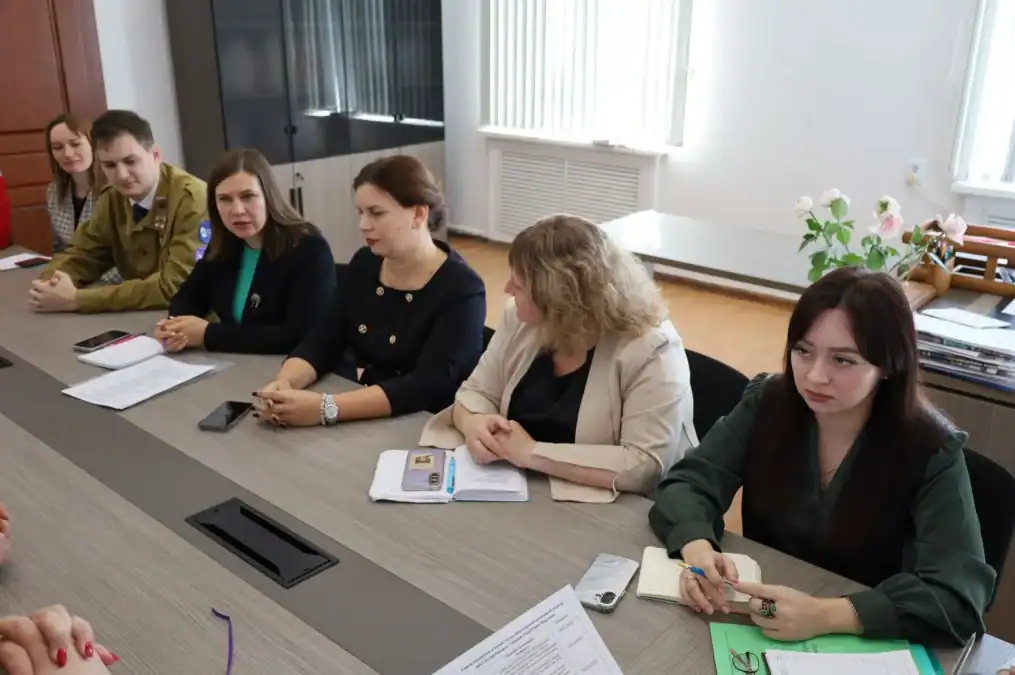 Участники встречи сидят за столом, перед ними блокноты и рабочие бумаги.