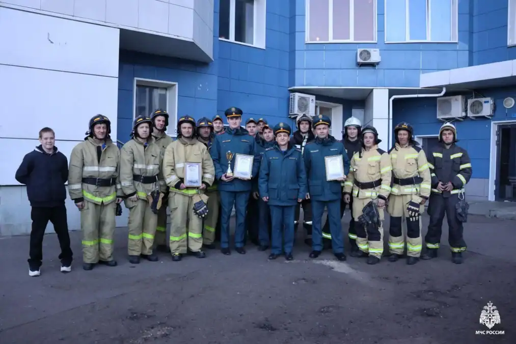 Группа спасателей и пожарных позирует у здания с грамотами.