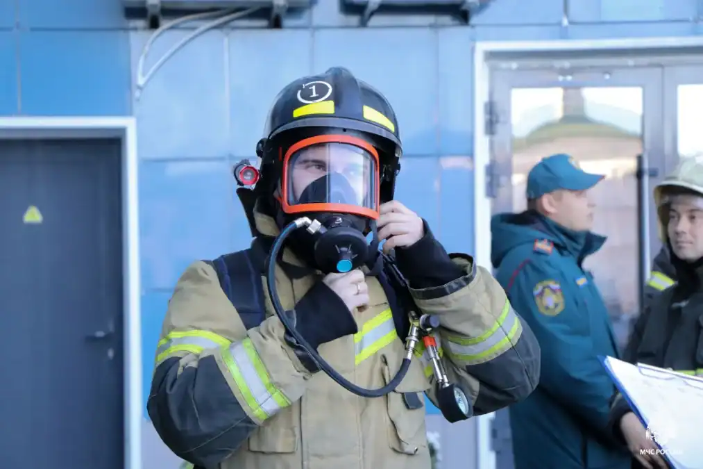 Пожарный поправляет маску дыхательного аппарата перед входом в здание.