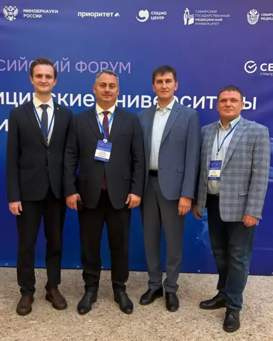 Четверо мужчин с бейджами стоят у синего стенда форума.