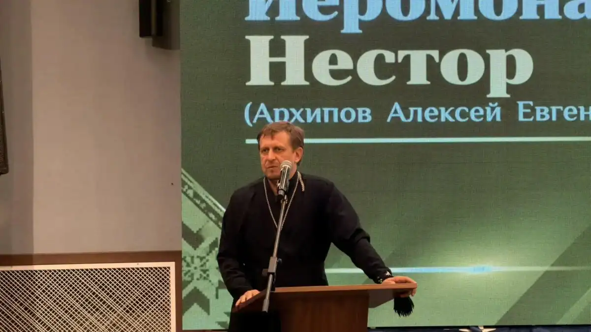 Иеромонах Нестор выступает за трибуной перед экраном с его именем.