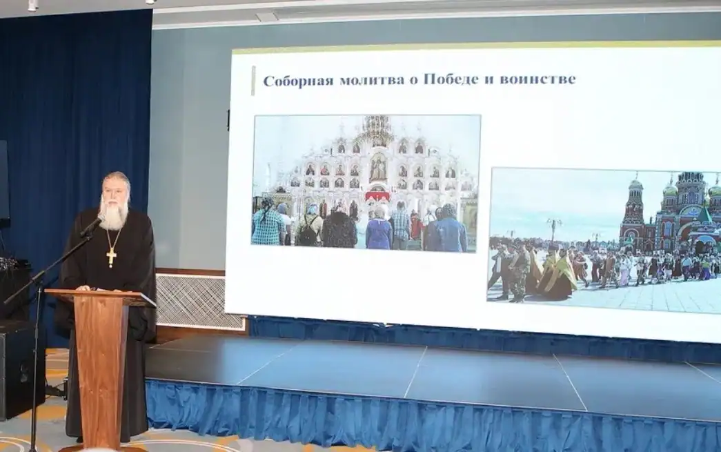 Священнослужитель выступает у трибуны рядом со слайдом о соборной молитве.