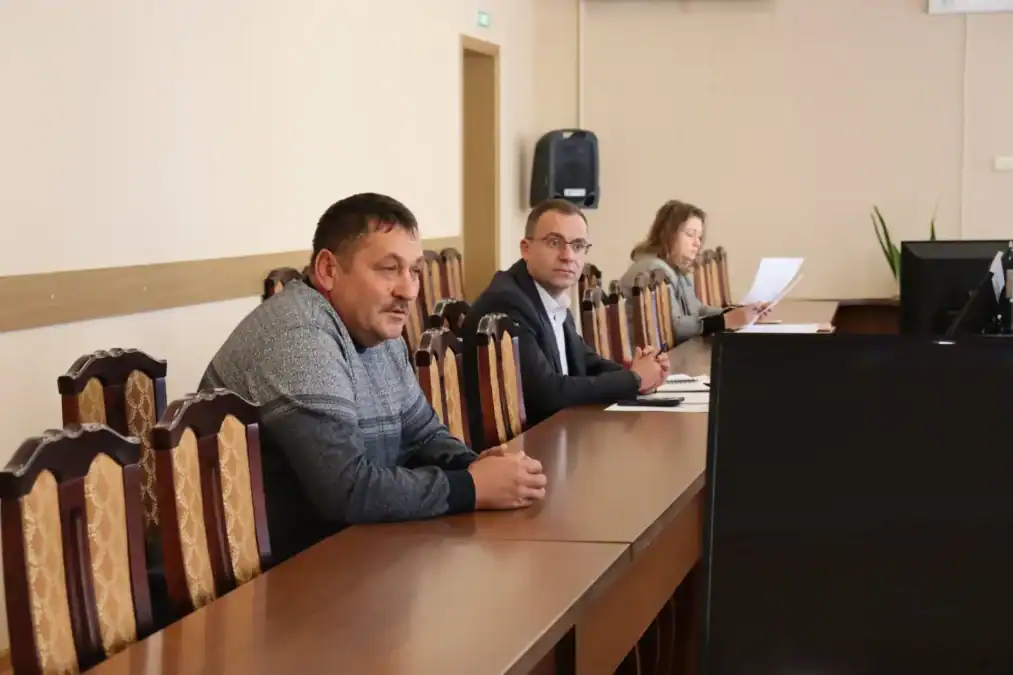 Трое участников заседания сидят за длинным столом с документами.
