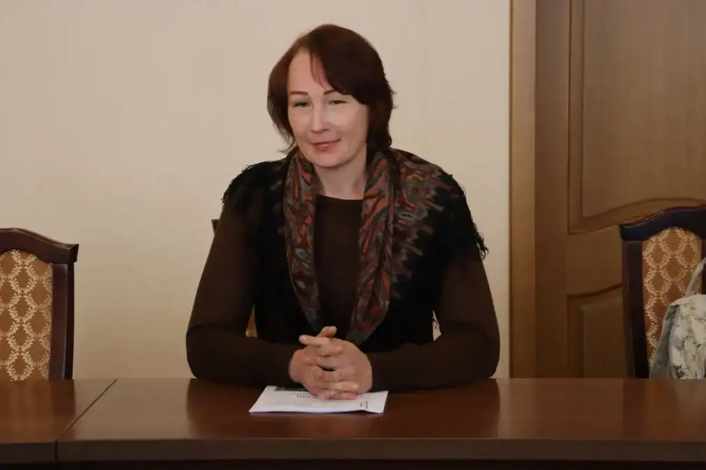 Женщина сидит за столом с листами документов перед собой.