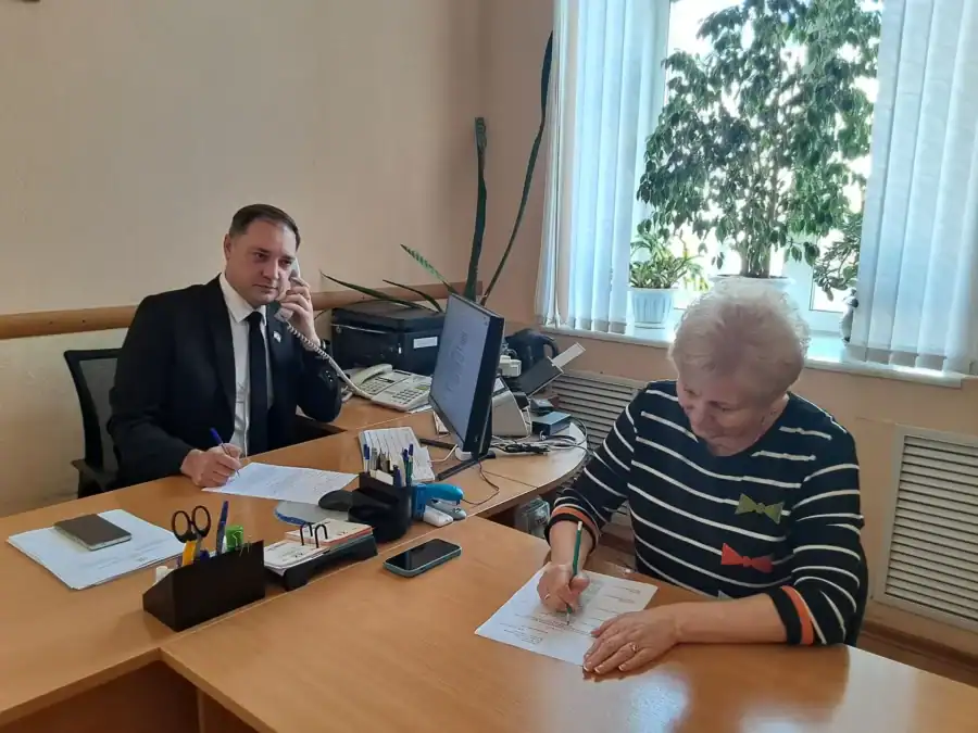 Мужчина за рабочим столом разговаривает по телефону, женщина пишет заявление.