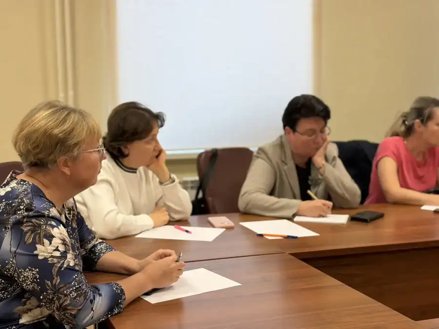 Четверо участников совещания делают записи и слушают обсуждение за столом.