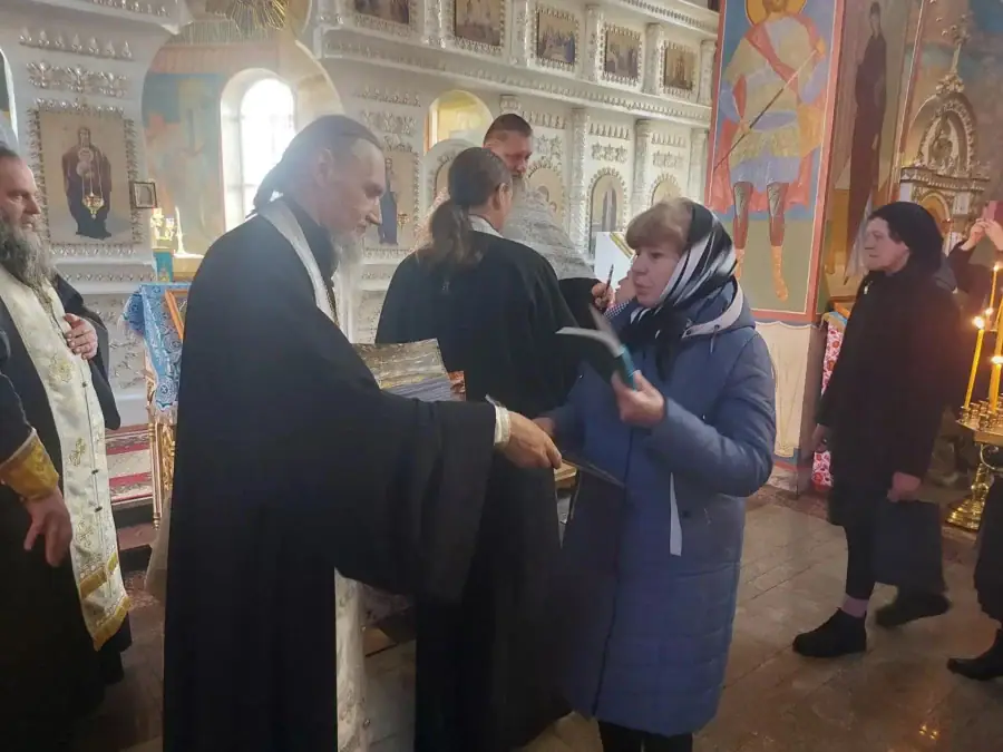 Священнослужитель передаёт женщине книгу в храме при других прихожанах.