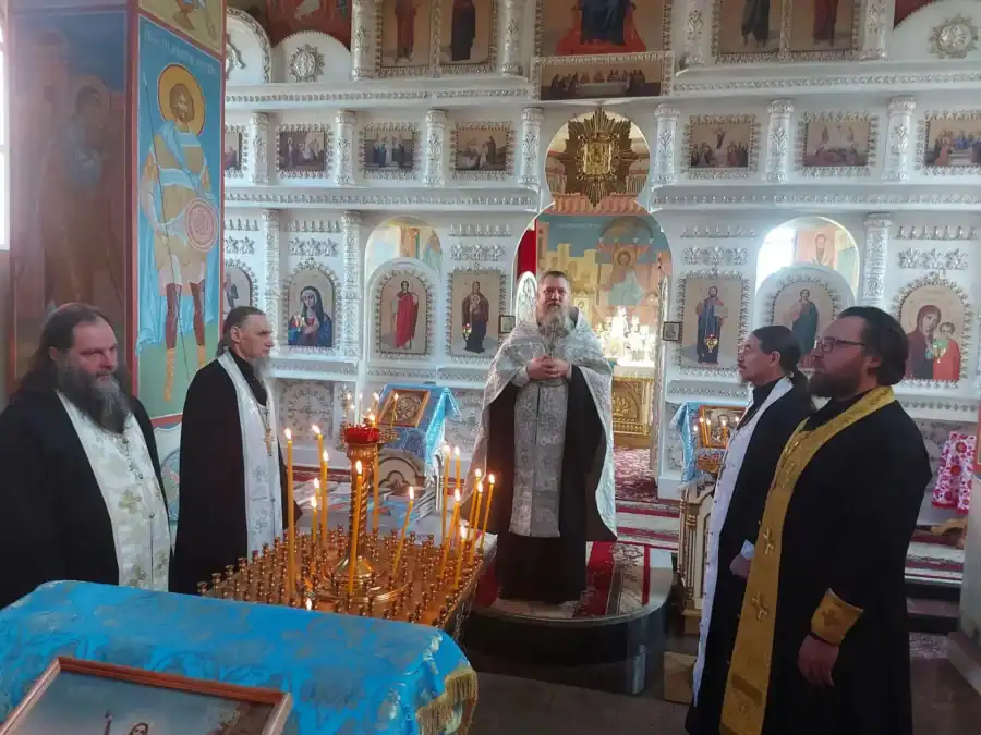 Несколько священнослужителей стоят перед алтарём в храме со свечами.