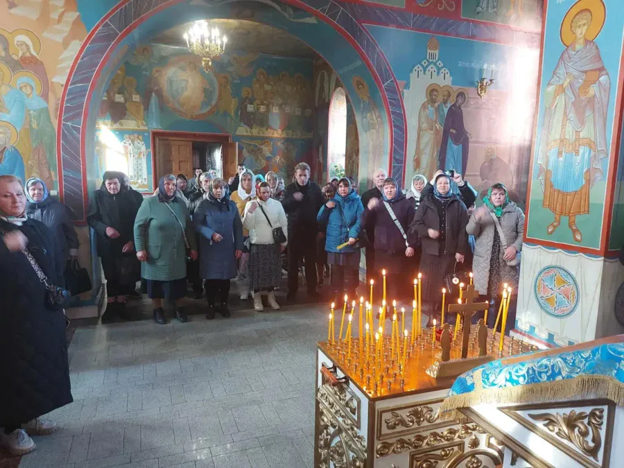 Прихожане стоят у свечного подсвечника в храме с настенными росписями.