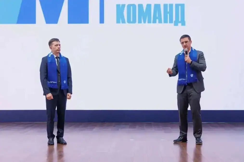 Двое мужчин в синих шарфах выступают на сцене с микрофоном.