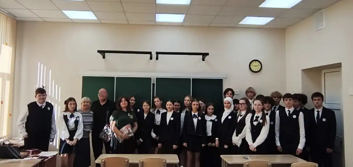Группа школьников и взрослых стоит перед доской в учебном классе.