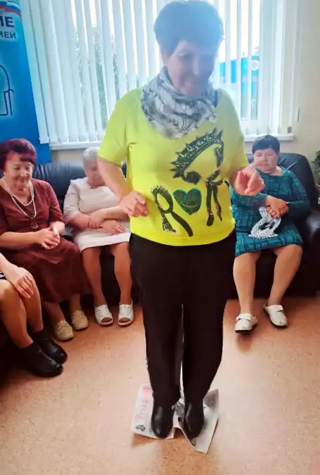 Женщина стоит на листах бумаги, а другие участницы сидят рядом.