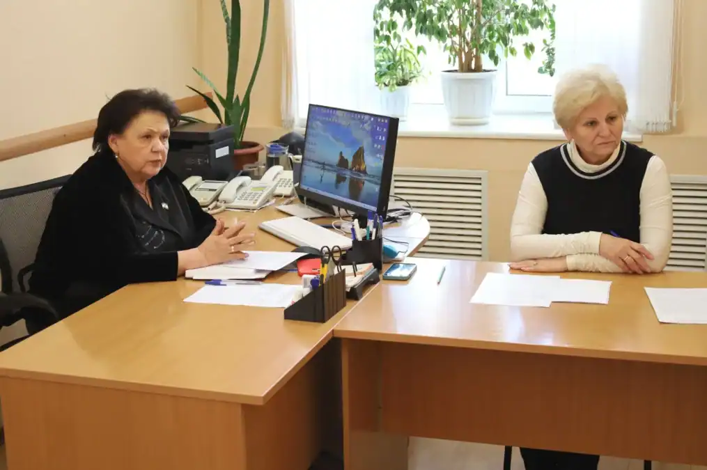 Две женщины сидят за рабочими столами в офисе с документами.