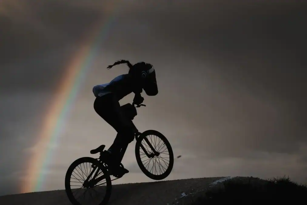 Силуэт BMX-райдера едет по гребню трассы на фоне радуги.