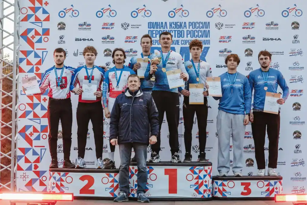 Группа спортсменов с медалями и грамотами стоит на пьедестале.