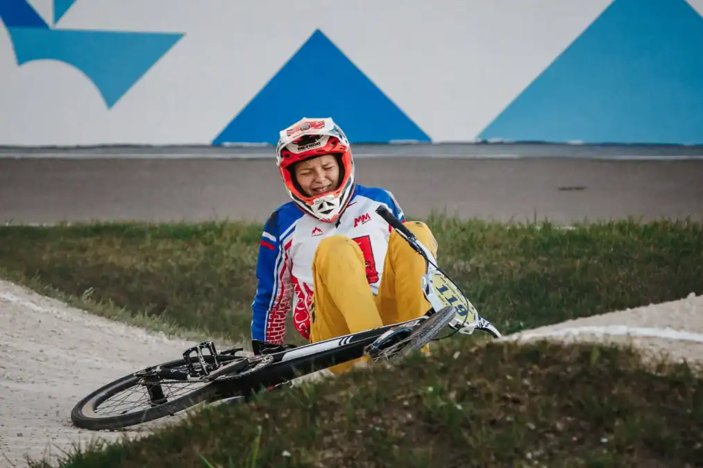 BMX-райдер сидит у края трассы рядом с упавшим велосипедом.
