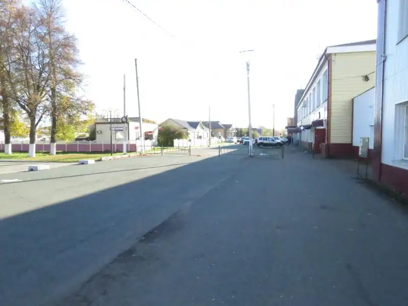 Городская улица с тротуаром, зданиями и несколькими автомобилями вдали.