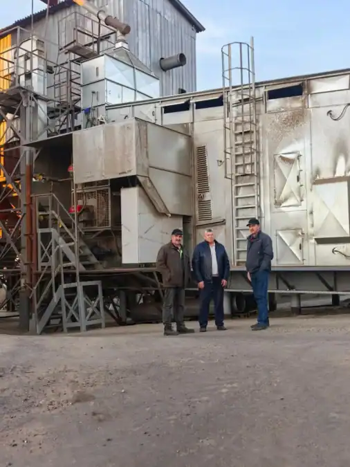 Трое мужчин стоят у крупной промышленной зерносушильной установки.