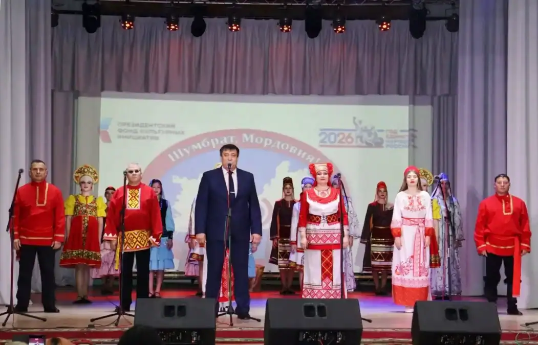 Артисты в народных костюмах стоят на сцене у микрофонов.