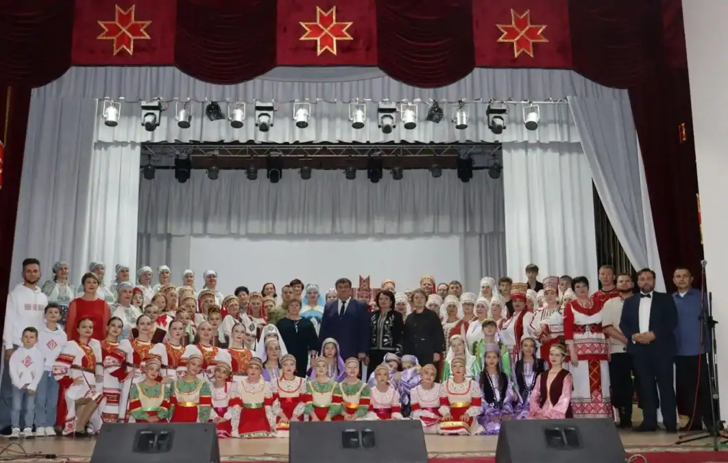 Участники фестиваля в национальных костюмах позируют на сцене.