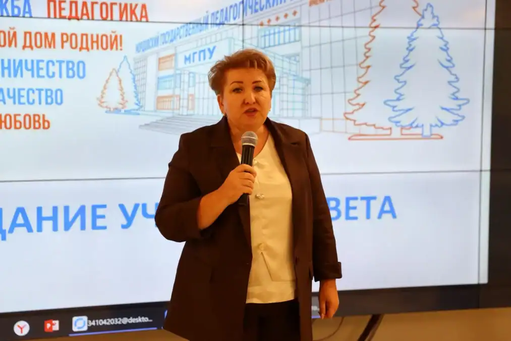 Женщина с микрофоном выступает на фоне экрана с символикой университета.