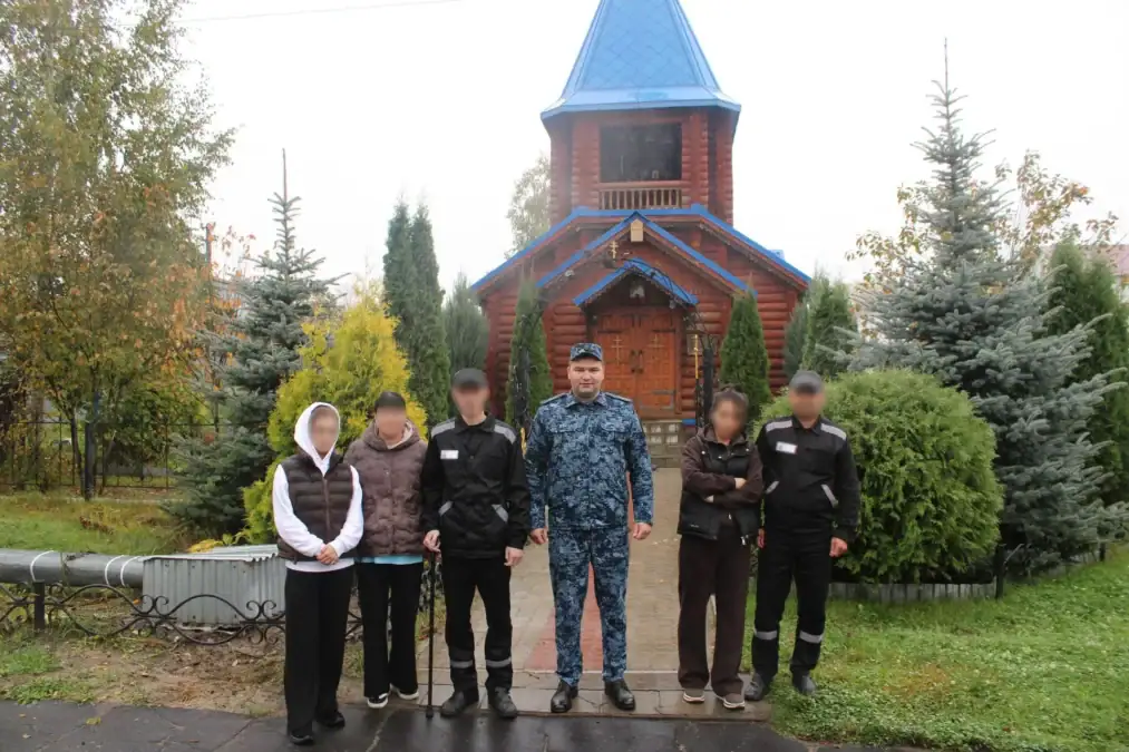 Сотрудник в форме и несколько посетителей стоят у кирпичного храма.